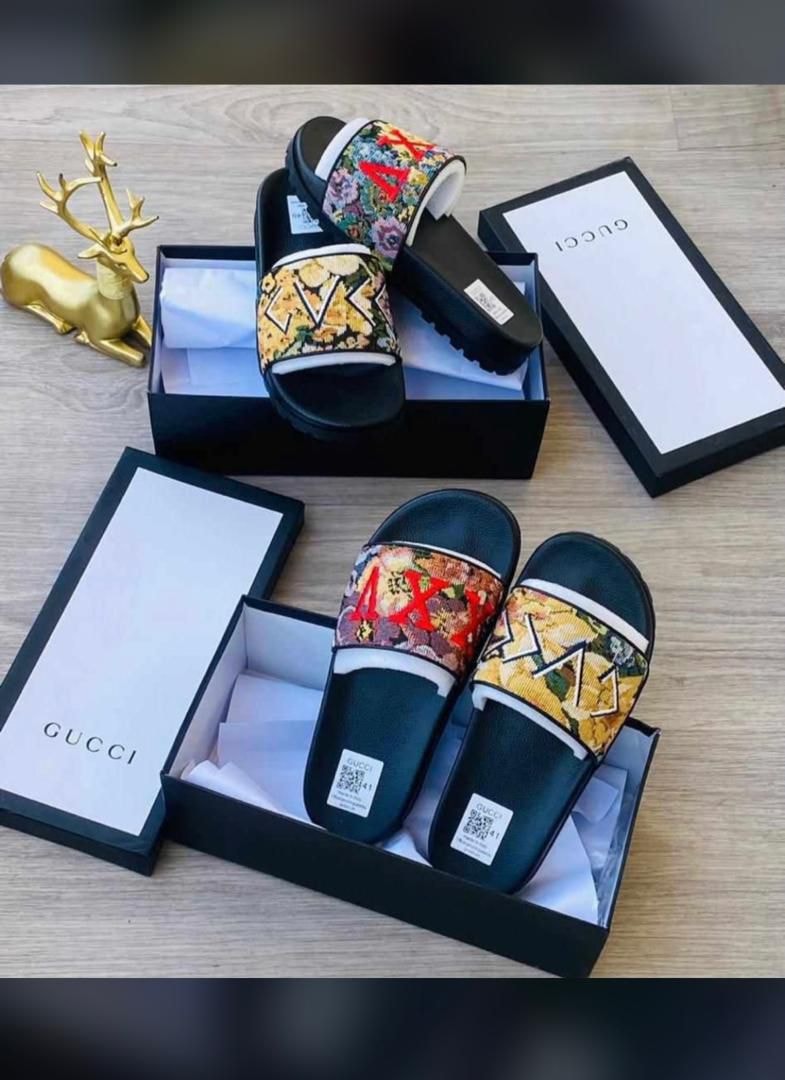 Gucci floral slides displayed in black boxes on wooden surface with gold decor.