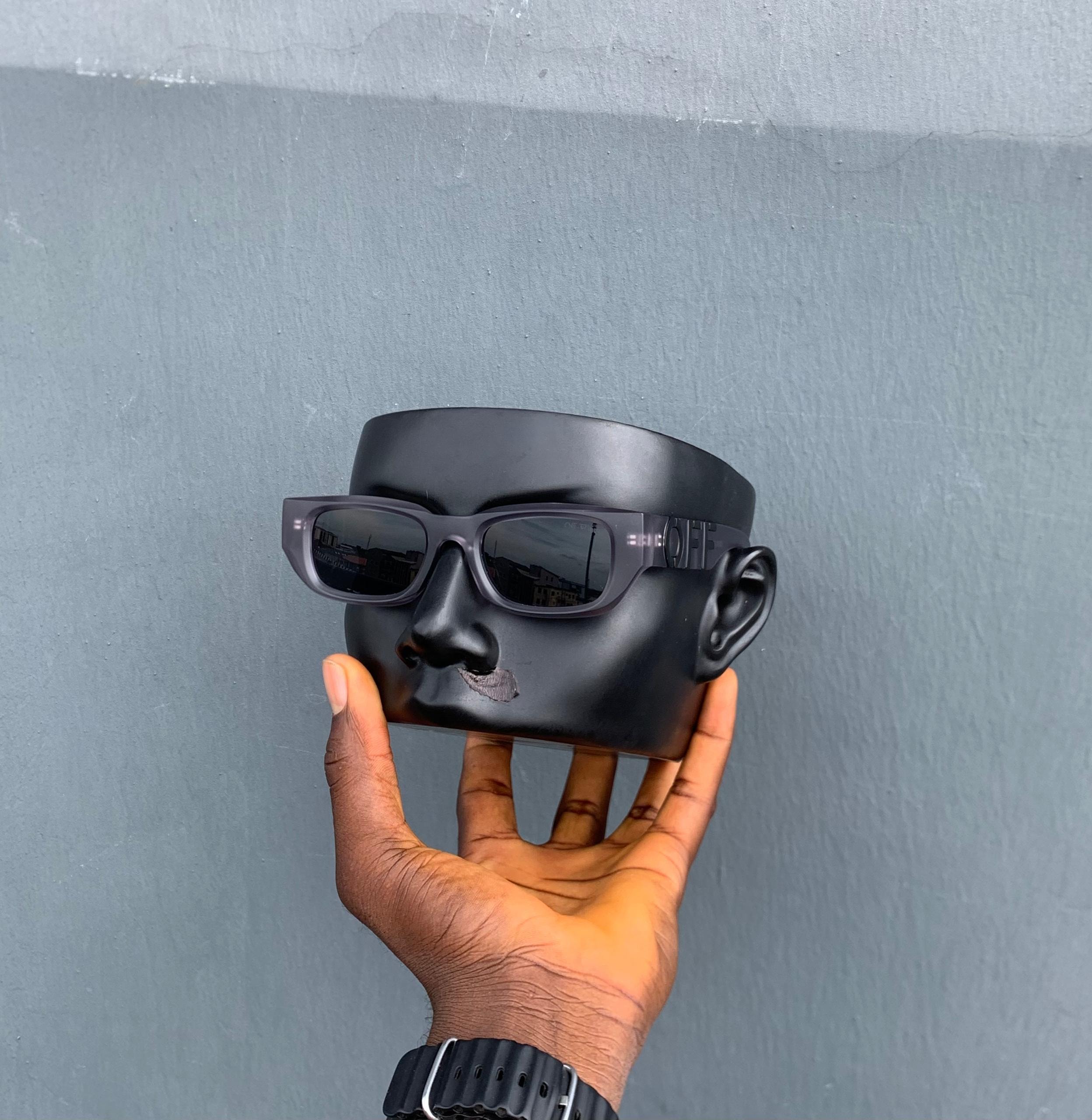 Off-White black sunglasses on a black mannequin head against gray wall.