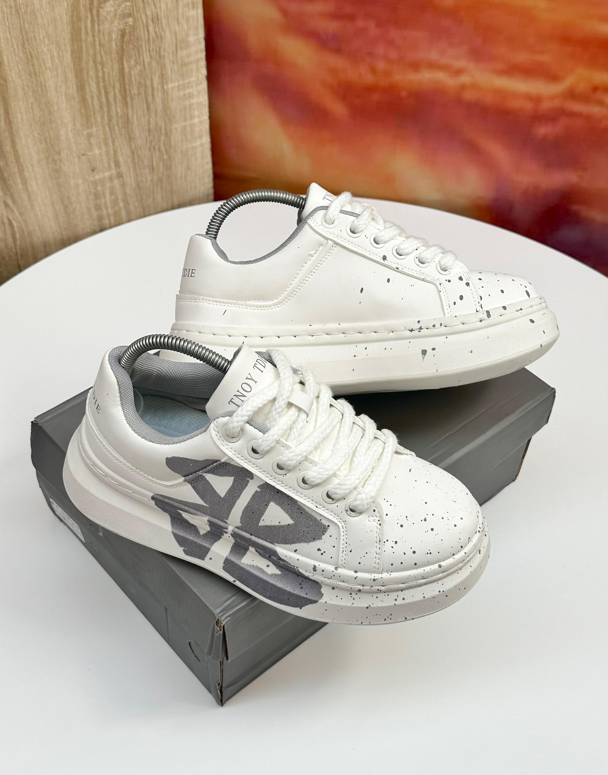 White TNOY TDIE sneakers with grey graphics and black speckles displayed on grey box.