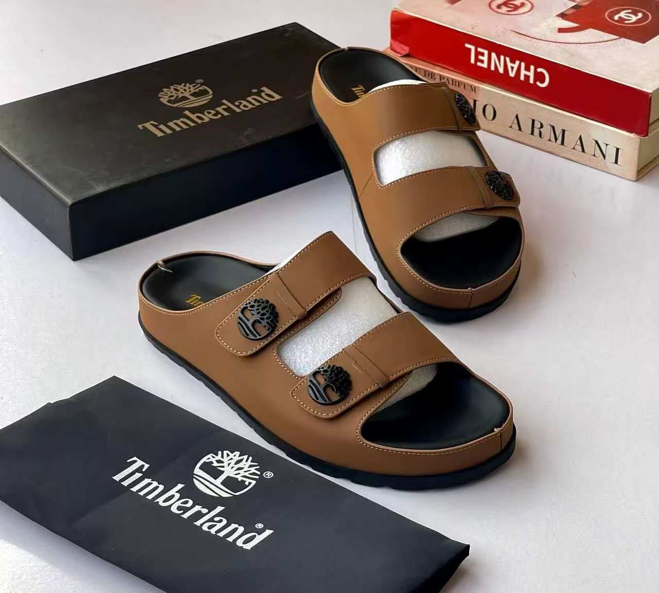 Brown Timberland double-strap sandals with tree logo, shown with black brand box and dustbag.