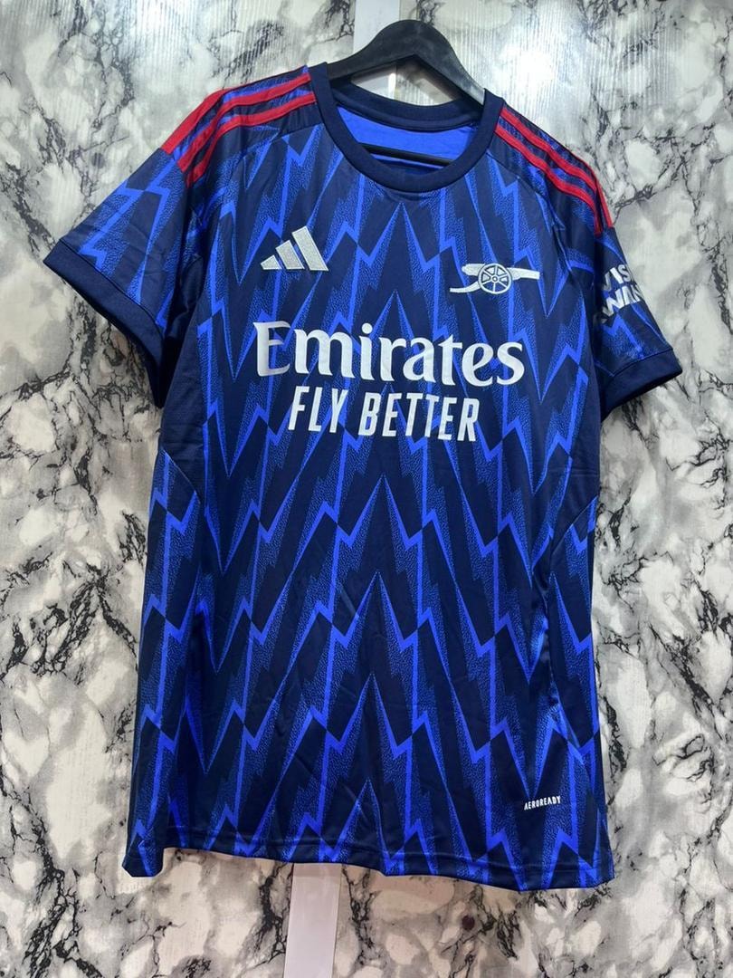 Blue Arsenal soccer jersey with zigzag pattern and Emirates branding on marble background.