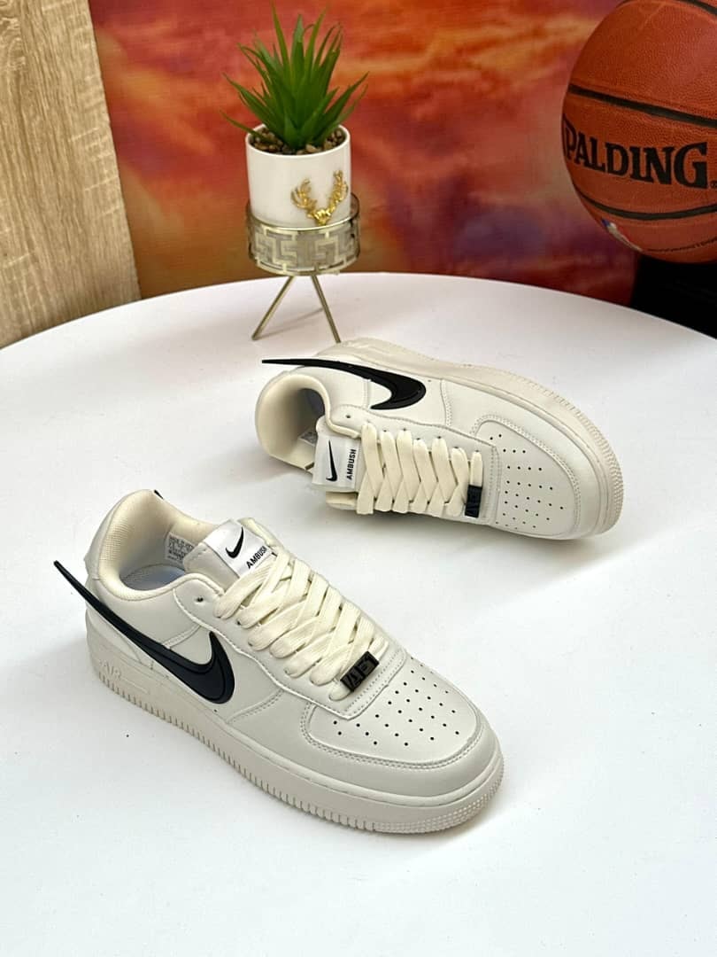 White Nike Air Force 1 Ambush edition with black swoosh on white surface with plant and basketball.