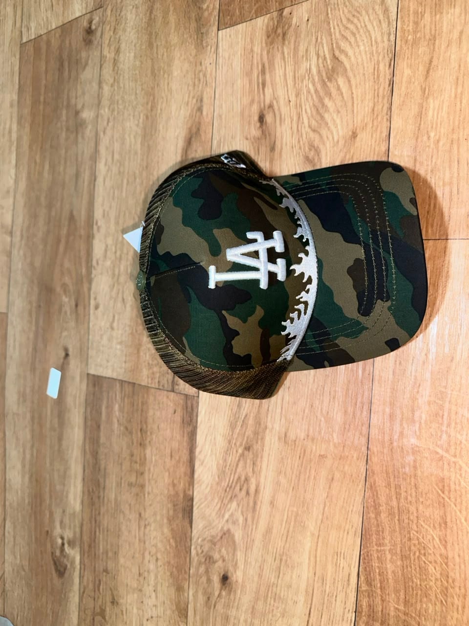 Camo trucker baseball cap with white LA logo and flame trim.