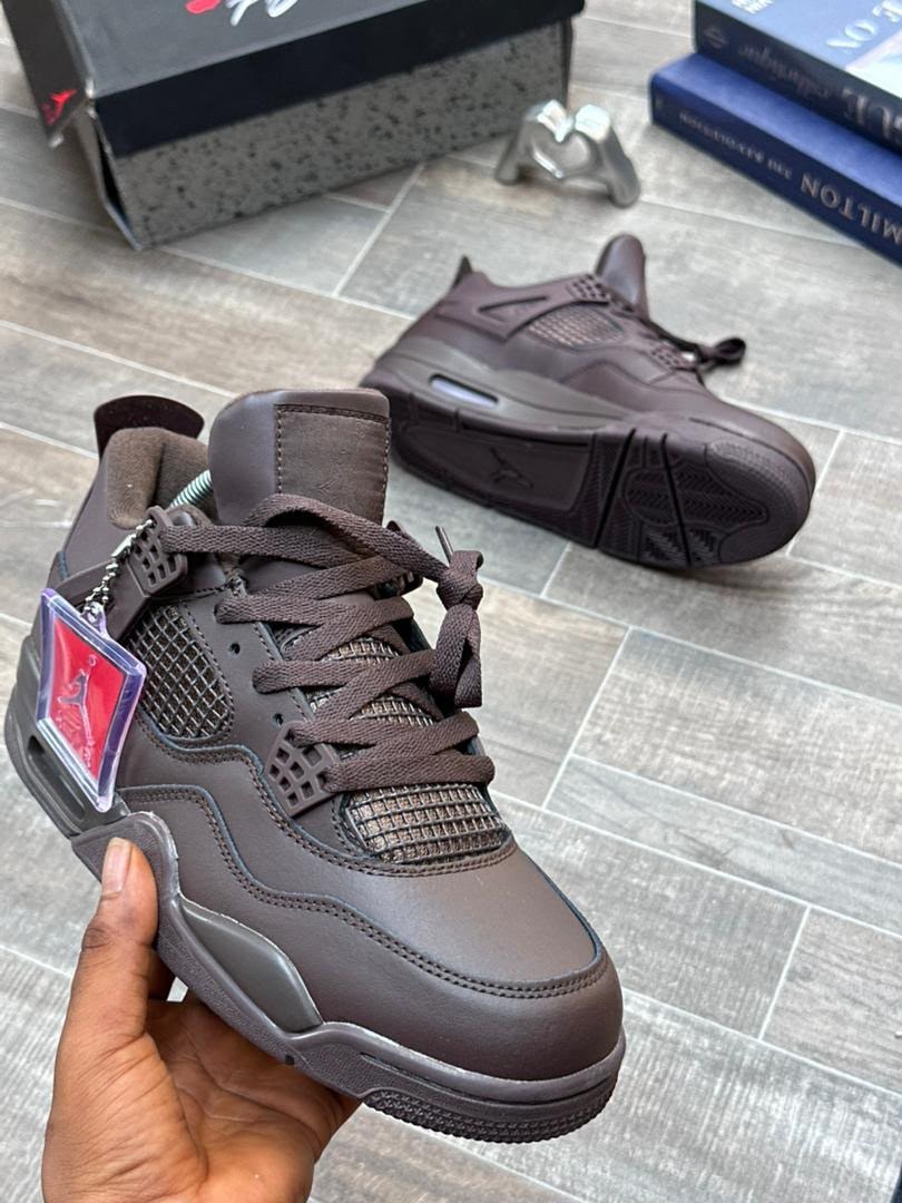 Brown Air Jordan 4 Retro sneaker held in hand with second pair in background.