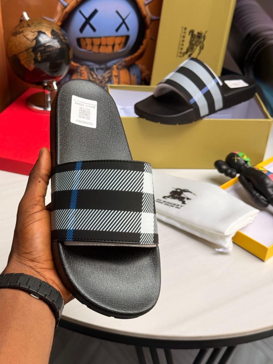 Burberry slides with plaid strap held showing pattern and logo.