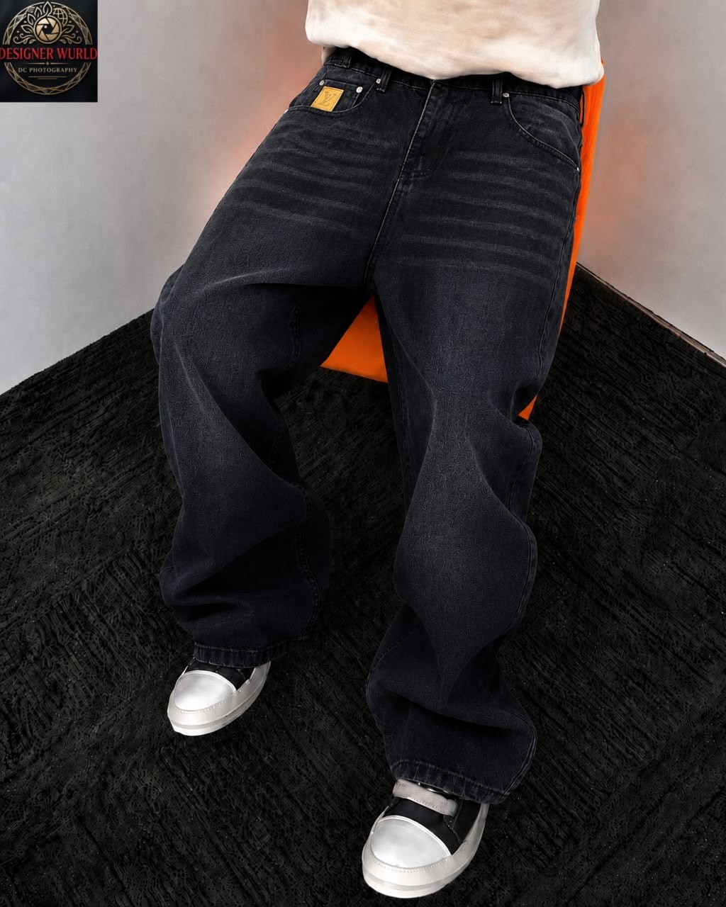 Model seated wearing black baggy jeans with back pocket patch and white top.