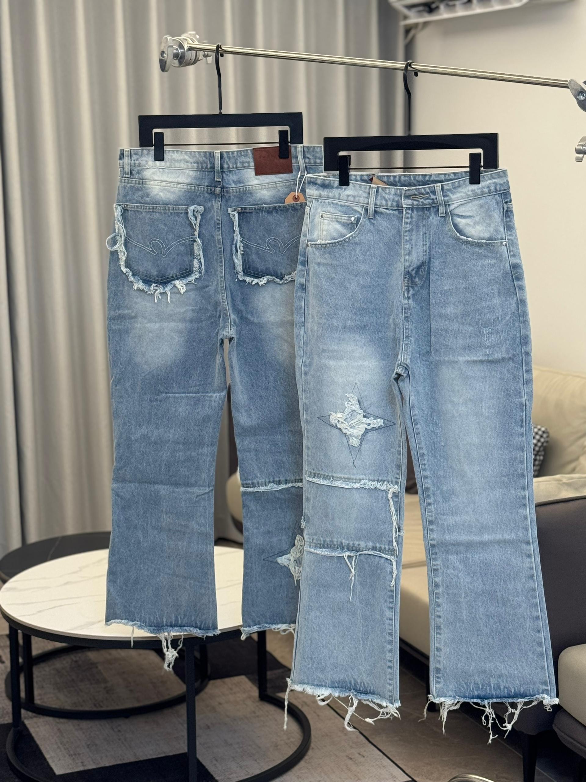 Light blue distressed baggy jeans with star patch, rips, and frayed hems, shown hanging.
