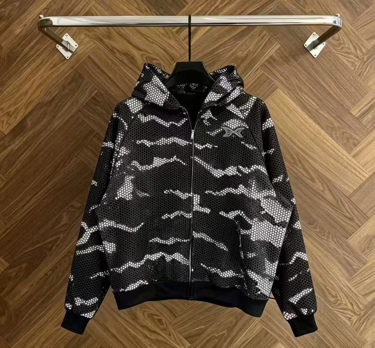 Black camo mesh zip-up hoodie on hanger against wooden background.