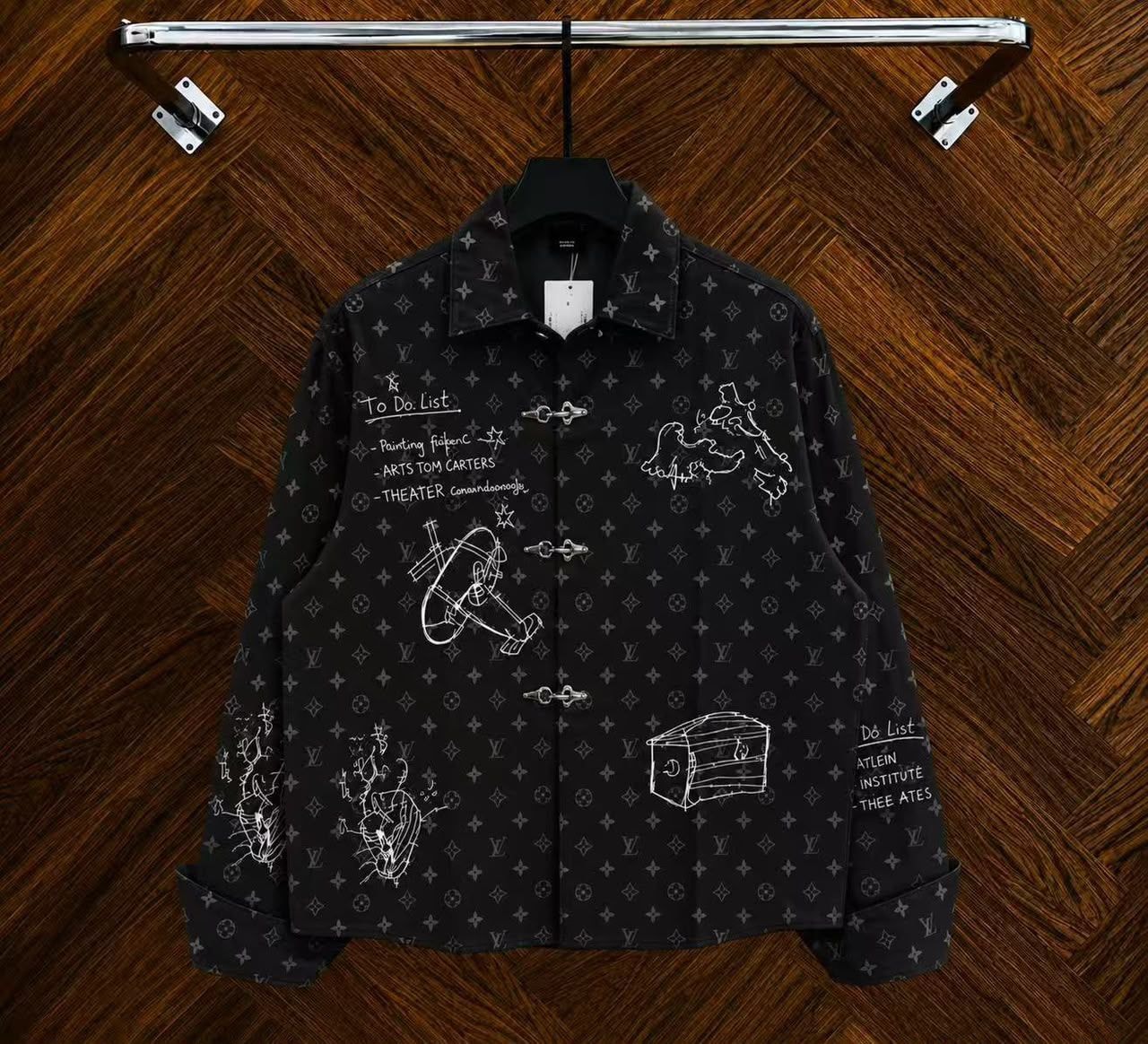 Black monogram sketch toggle jacket hanging on rack with white drawings.