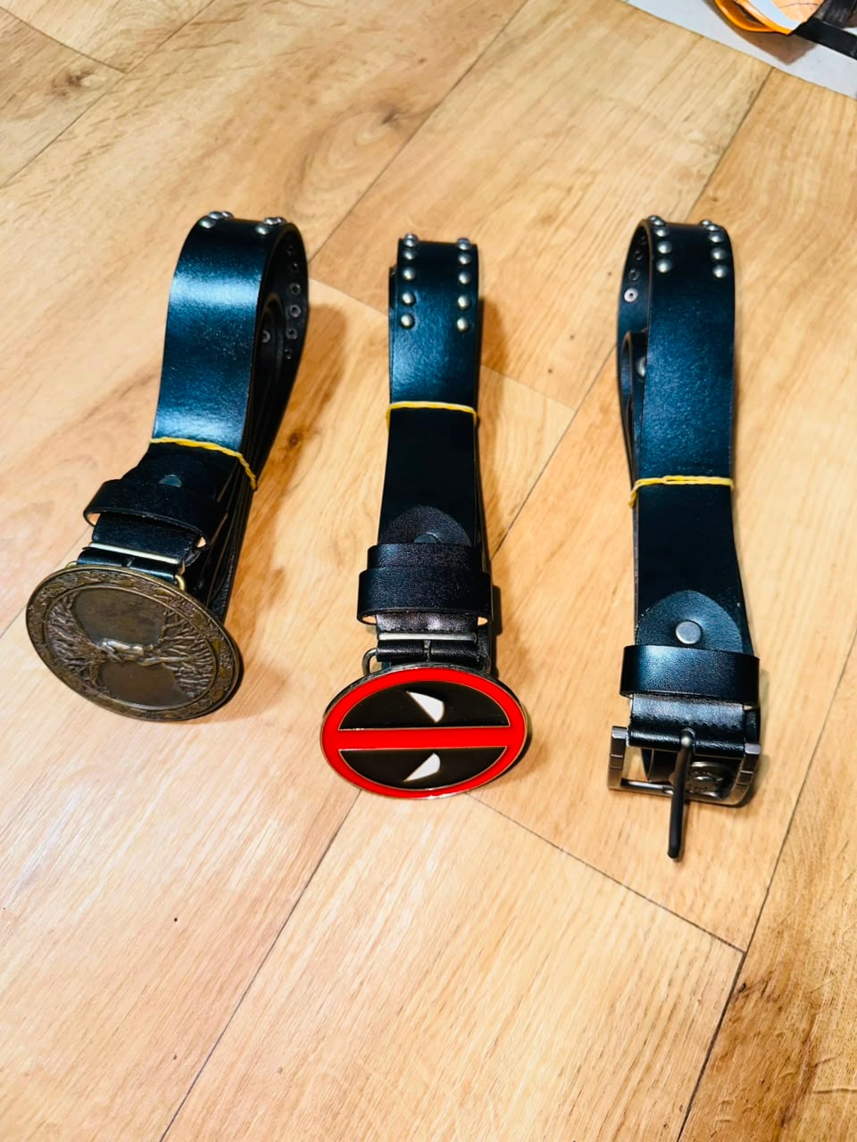 Three black leather belts with embossed, graphic, and studded buckles.