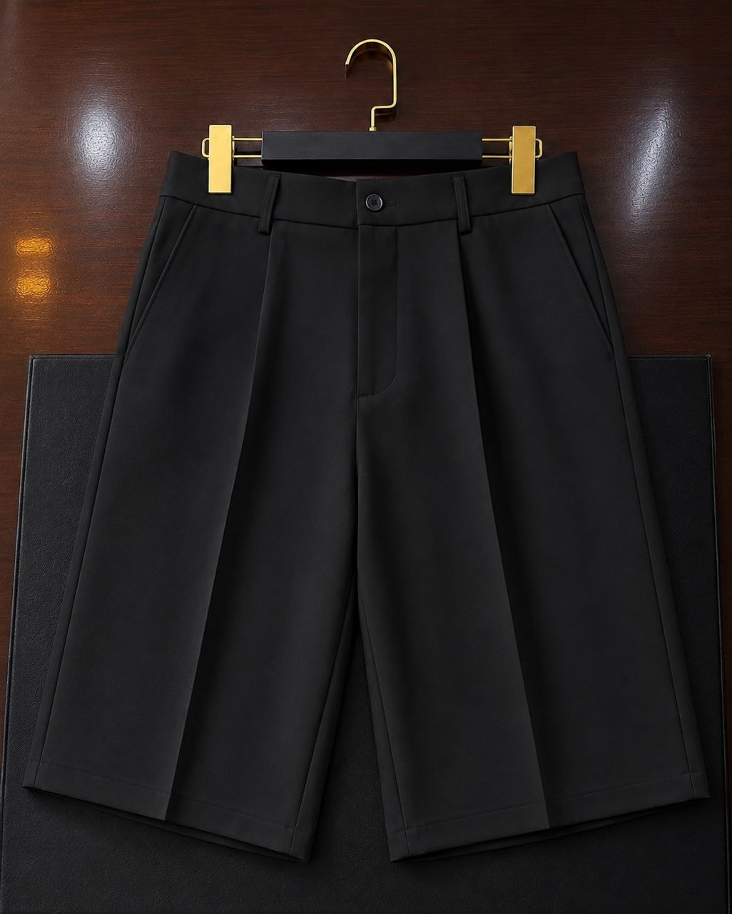 Black tailored pleated shorts flat lay on wooden surface.