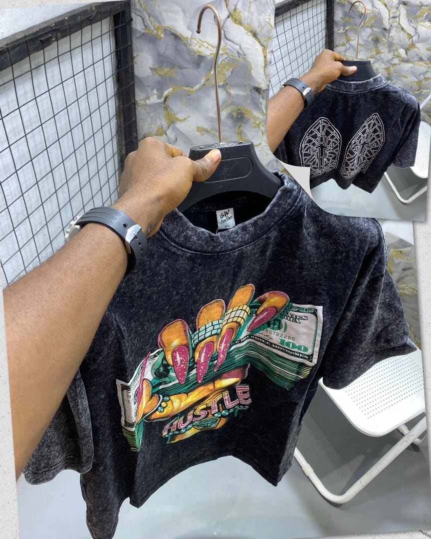 Black stone wash t-shirt held up showing front Hustle nails and money graphic with back wing design inset.