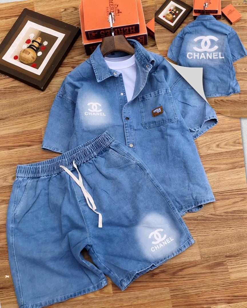 Flat lay of light blue denim shirt and shorts with white Chanel logos.