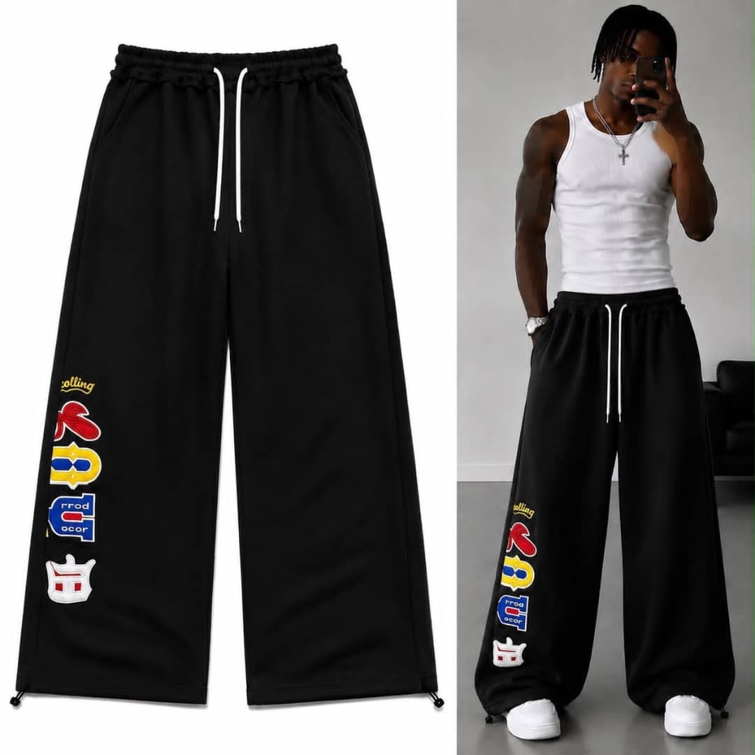 Black graphic print joggers on model in white tank top taking mirror selfie.