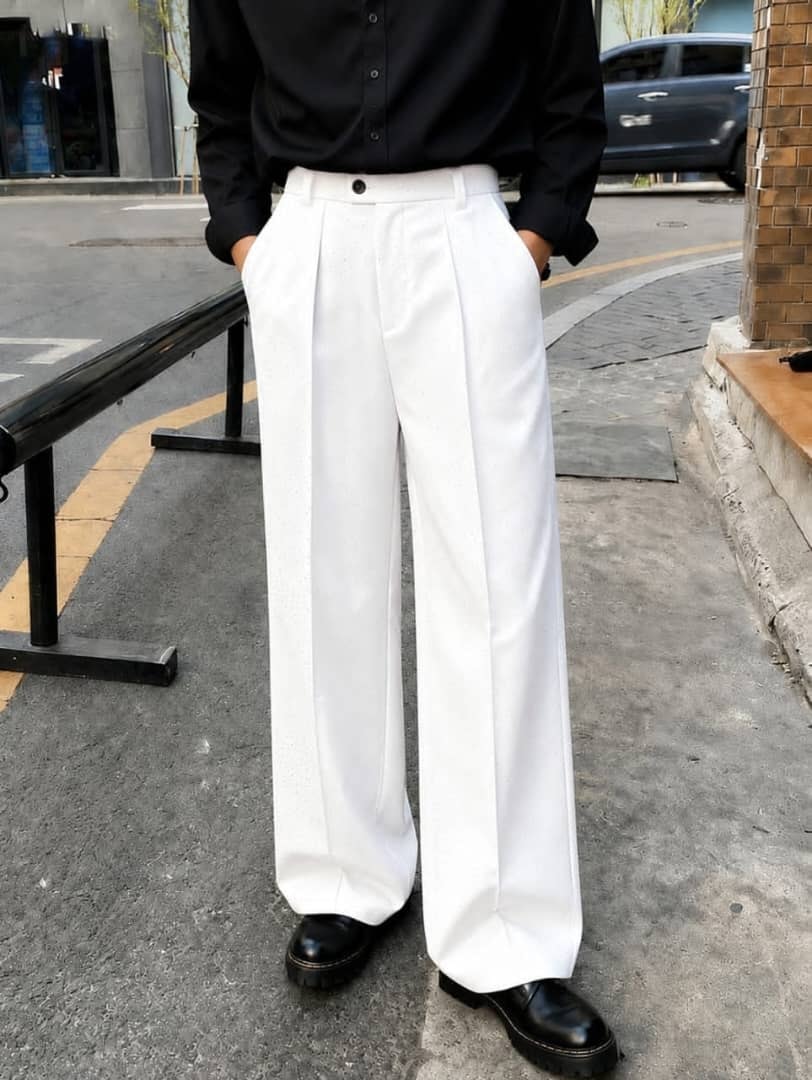 Model wearing white embellished wide-leg flare trousers with hands in pockets.