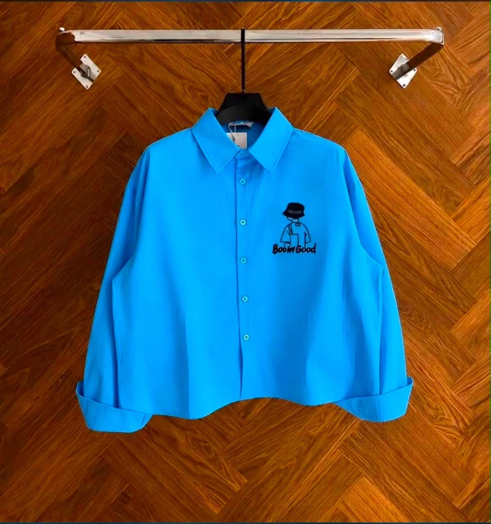 Front view of blue cropped button-up shirt with Boom Good chest embroidery.
