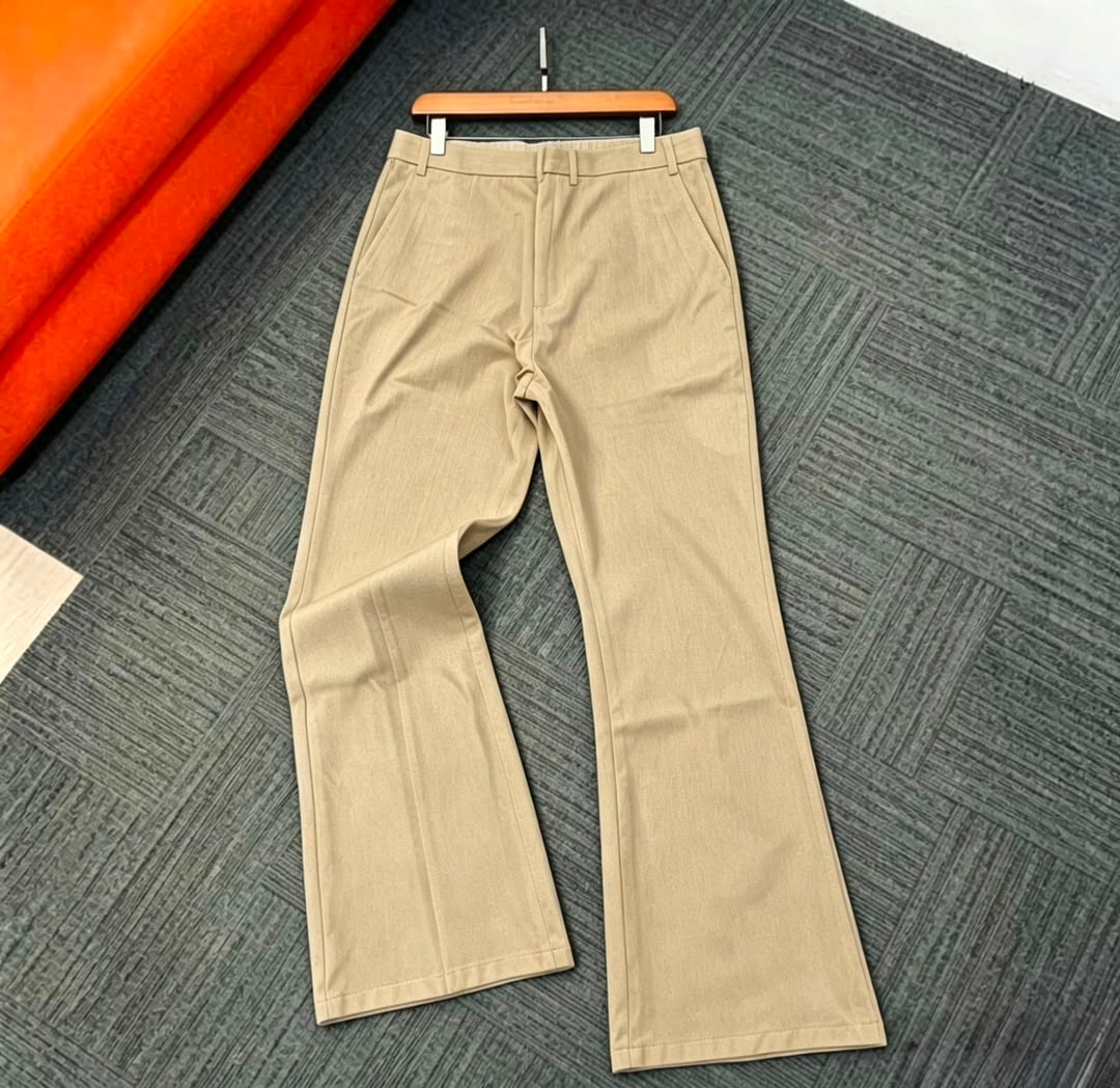 Beige flare trousers hung on wooden hanger with orange fabric in background.