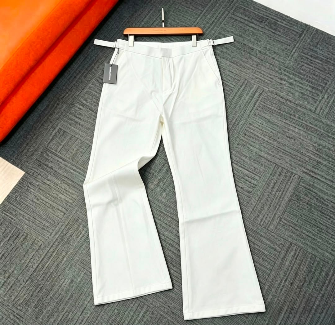 White flare trousers hung on wooden hanger over patterned floor.