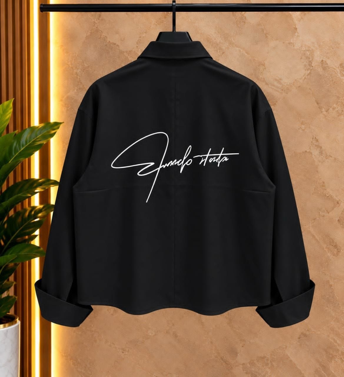Back view of black cropped toggle button shirt on hanger with white script embroidery.