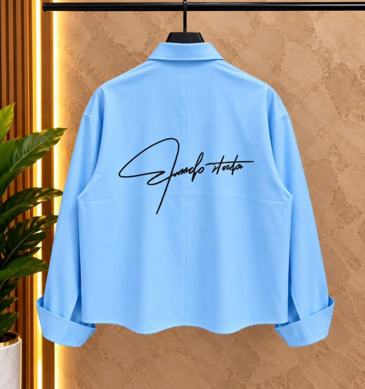 Back view of light blue cropped toggle button shirt on hanger showing large script embroidery.