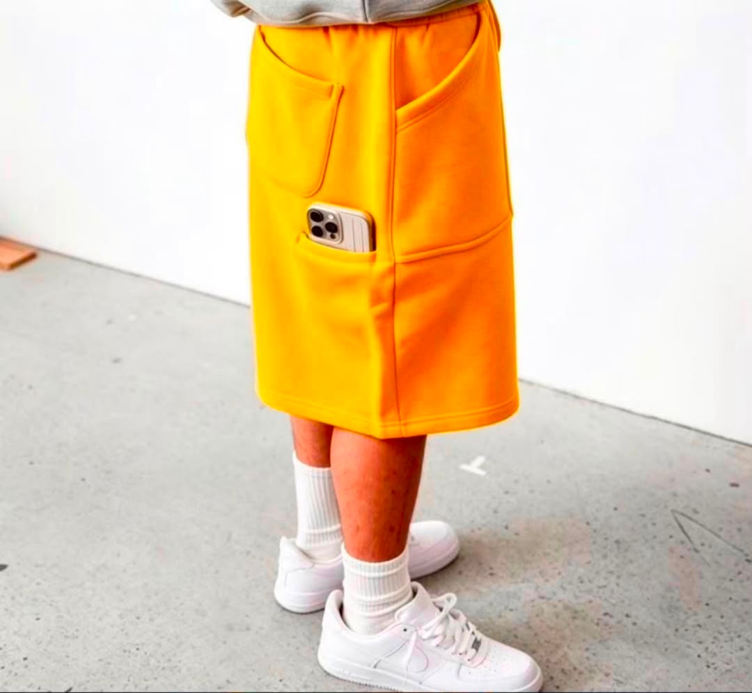 Model wearing yellow fleece shorts with phone in thigh pocket, styled with white sneakers.
