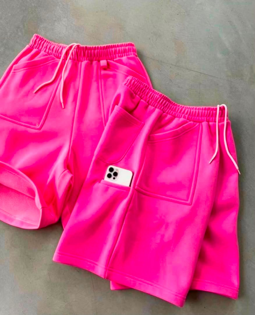 Bright pink fleece shorts laid flat showing drawstring waist and patch pocket.