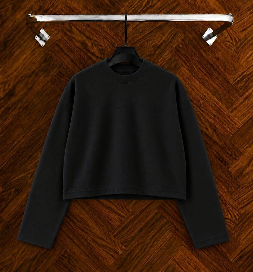 Black cropped long sleeve sweatshirt on hanger against wooden background.