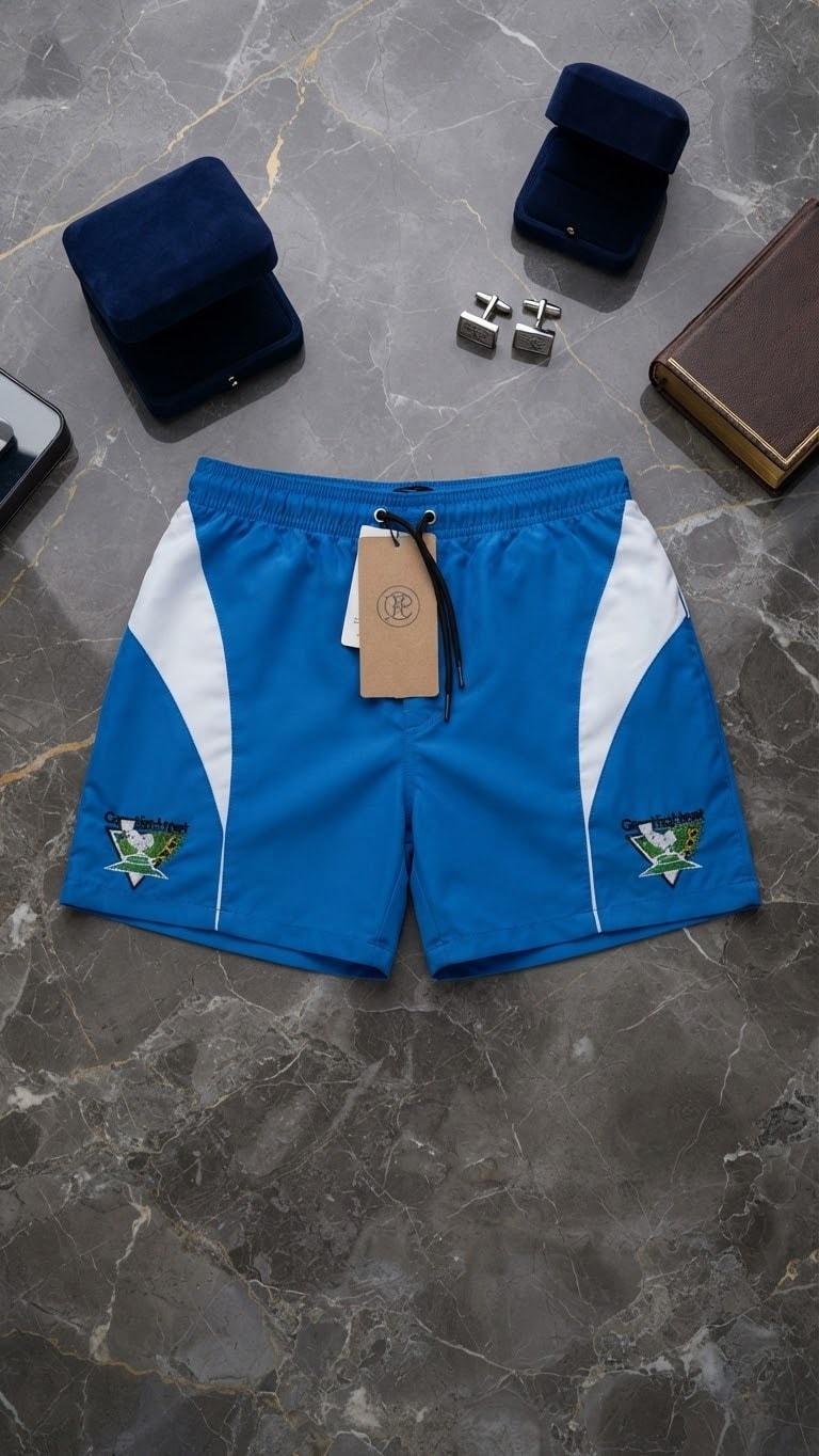 Blue contrast panel shorts with crest embroidery on marble background.