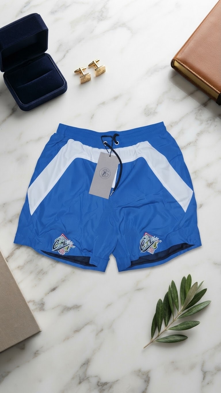 Blue contrast panel shorts with embroidered crests on marble surface.