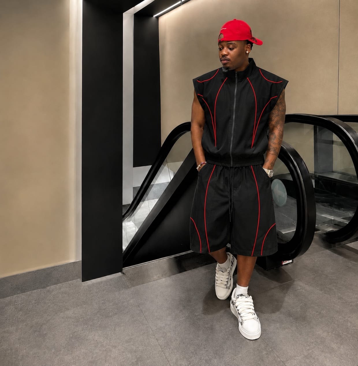Man modeling black sleeveless zip-up vest and shorts with red contrast piping.
