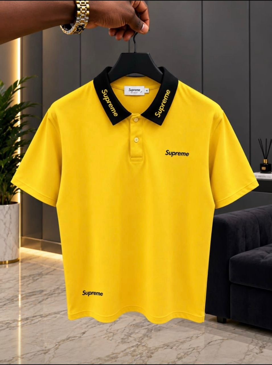Yellow Supreme polo shirt with black collar on hanger.