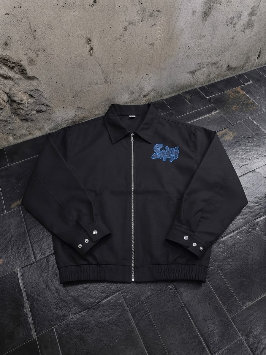 Black zip-up bomber jacket with blue chest embroidery laid flat on dark tiles.