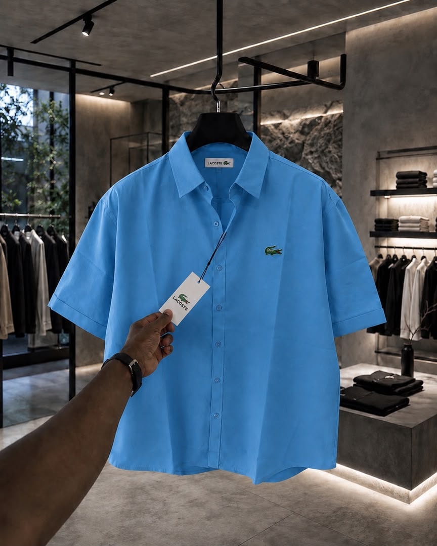 Blue Lacoste short sleeve button-up shirt with hand holding branded tag.