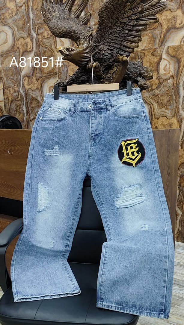 Light blue ripped baggy jeans with yellow black circular graphic patch on thigh.