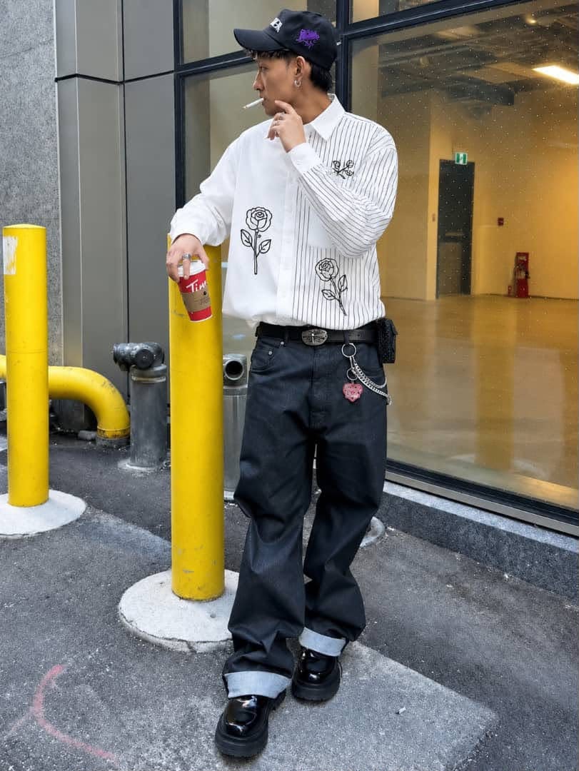 Man posing outdoors in white pinstriped shirt with black rose embroidery.