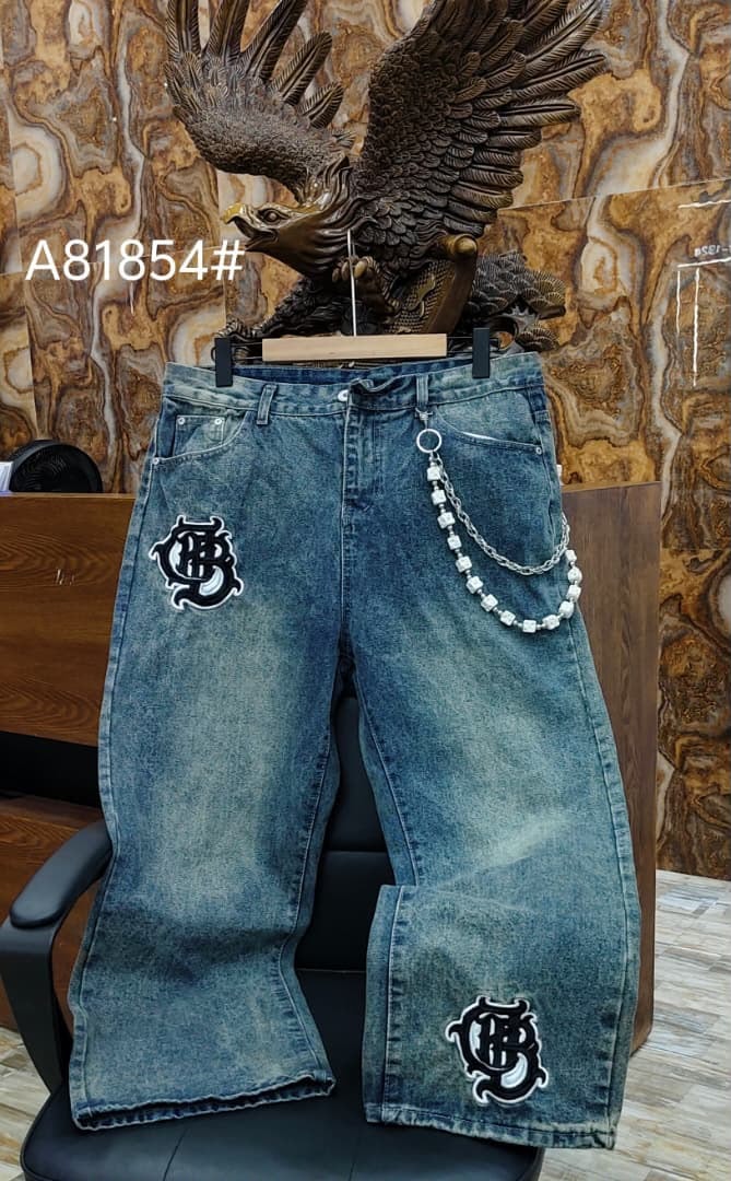Blue jeans with black and white gothic patches, beaded chain accessory, displayed on chair.