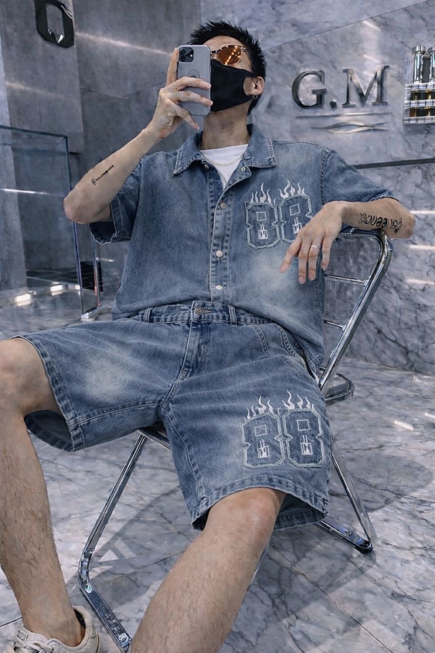 Man wearing light blue denim shirt and shorts with 88 flame embroidery.
