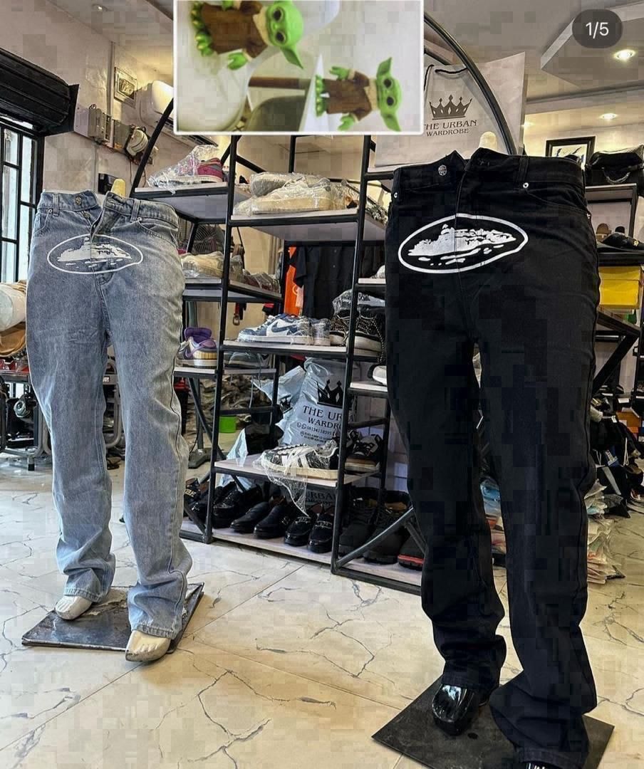 Two pairs of logo print baggy jeans on mannequins in store, one light blue and one black with white oval graphics.