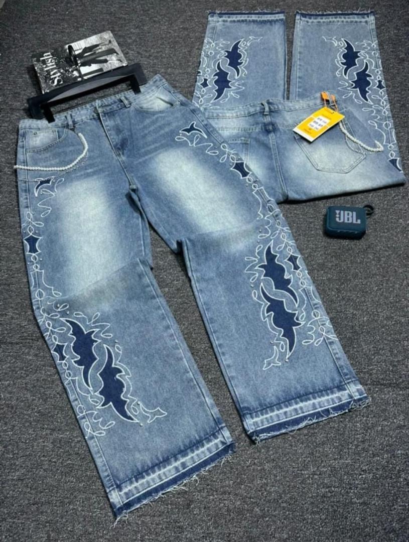 Light blue baggy jeans with blue and white embroidered patterns and frayed hems laid flat.