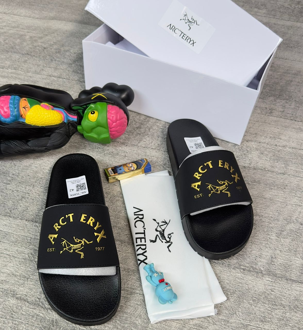 Arc'teryx black slides displayed with white box, dust bag, and accessories.