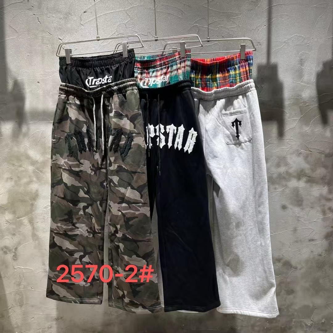Three Trapstar designer joggers in camouflage, black, and light grey shown side by side on hangers.