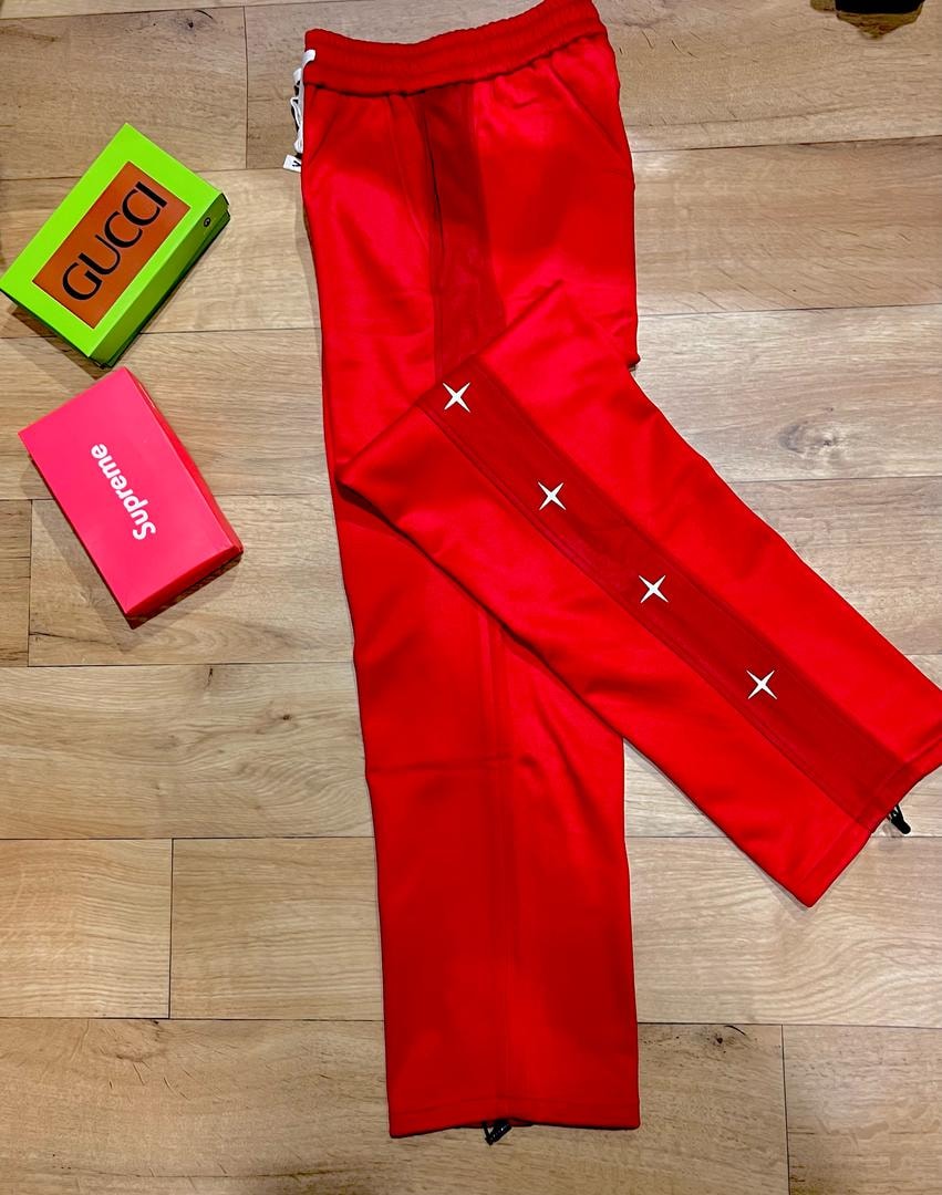 Red joggers with white cross embroidery on side panel laid flat on wood with Gucci and Supreme boxes.