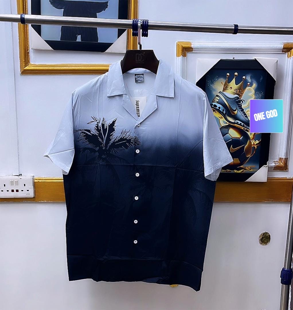 Blue gradient shirt with palm tree print hanging on clothing rack.