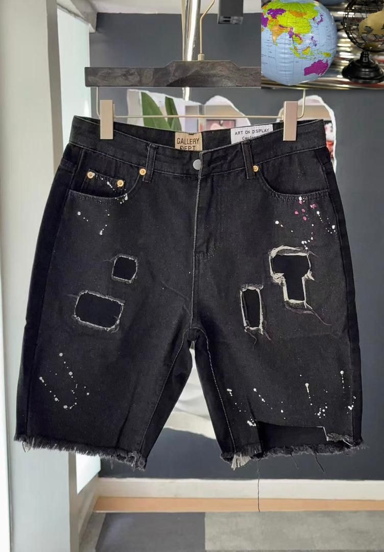 Black Gallery Dept denim shorts with paint splatter, rips and frayed hems on hanger.