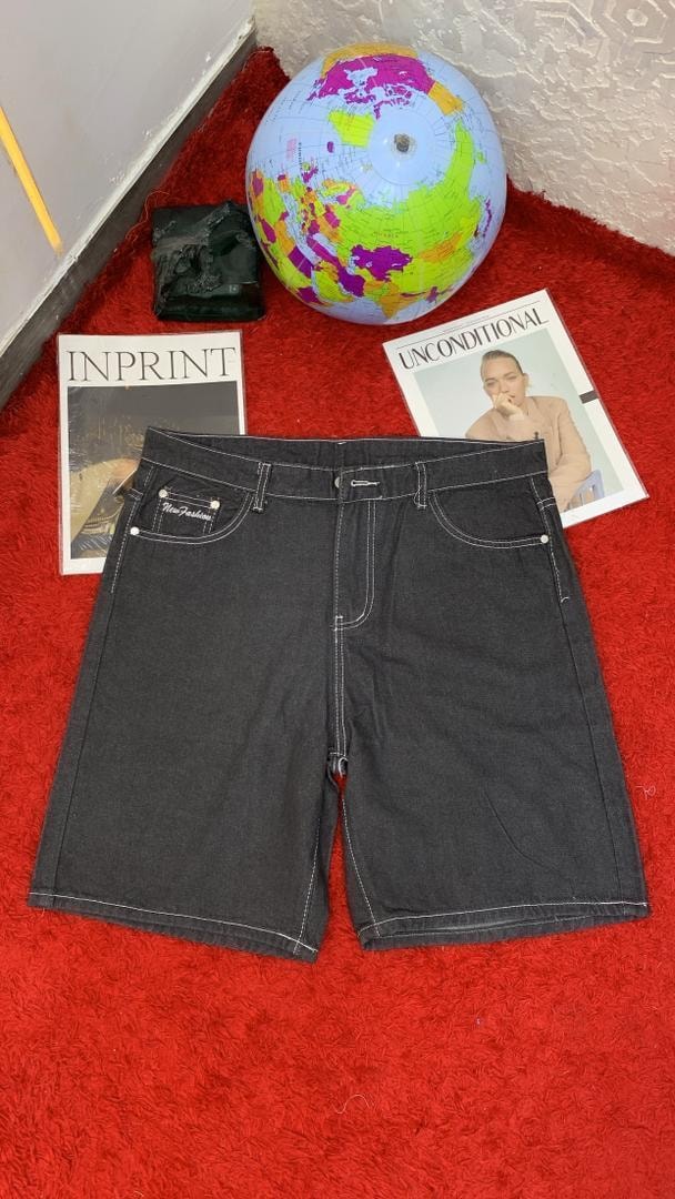 Black denim shorts with white contrast stitching laid flat on red surface.