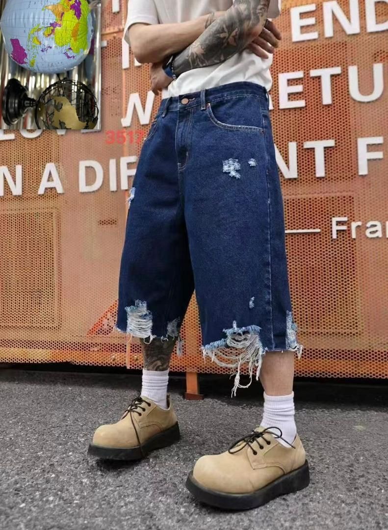 Model wearing navy blue baggy distressed denim shorts with rips and frayed hems.