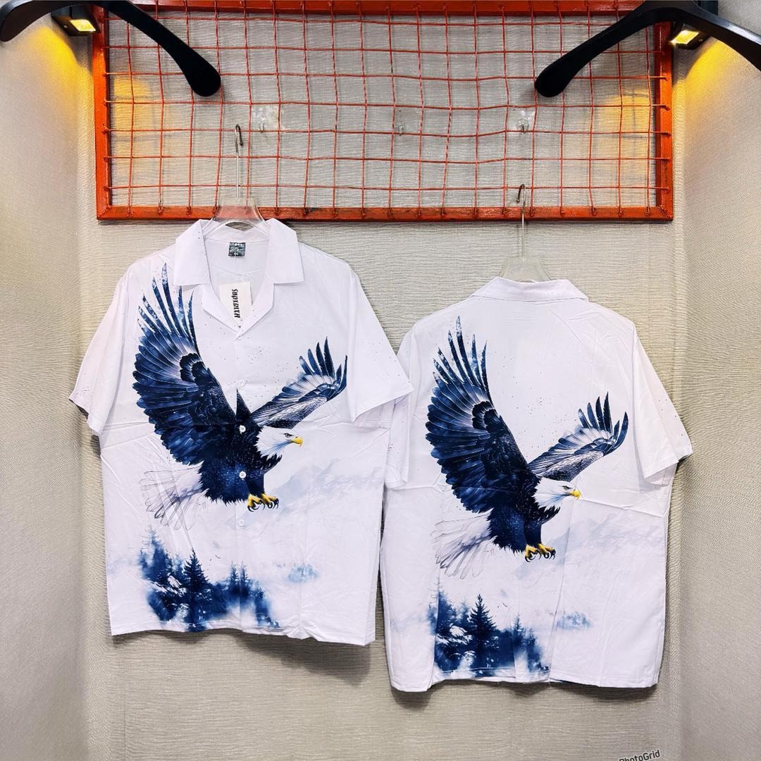 White short sleeve shirt with eagle graphic shown in front and back views hanging on wall.