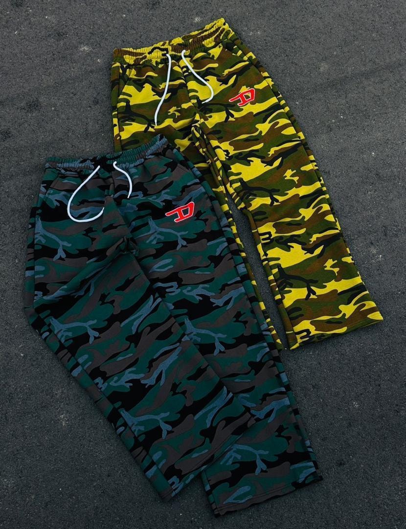 Green and yellow camouflage joggers laid out on dark pavement showing logo detail.