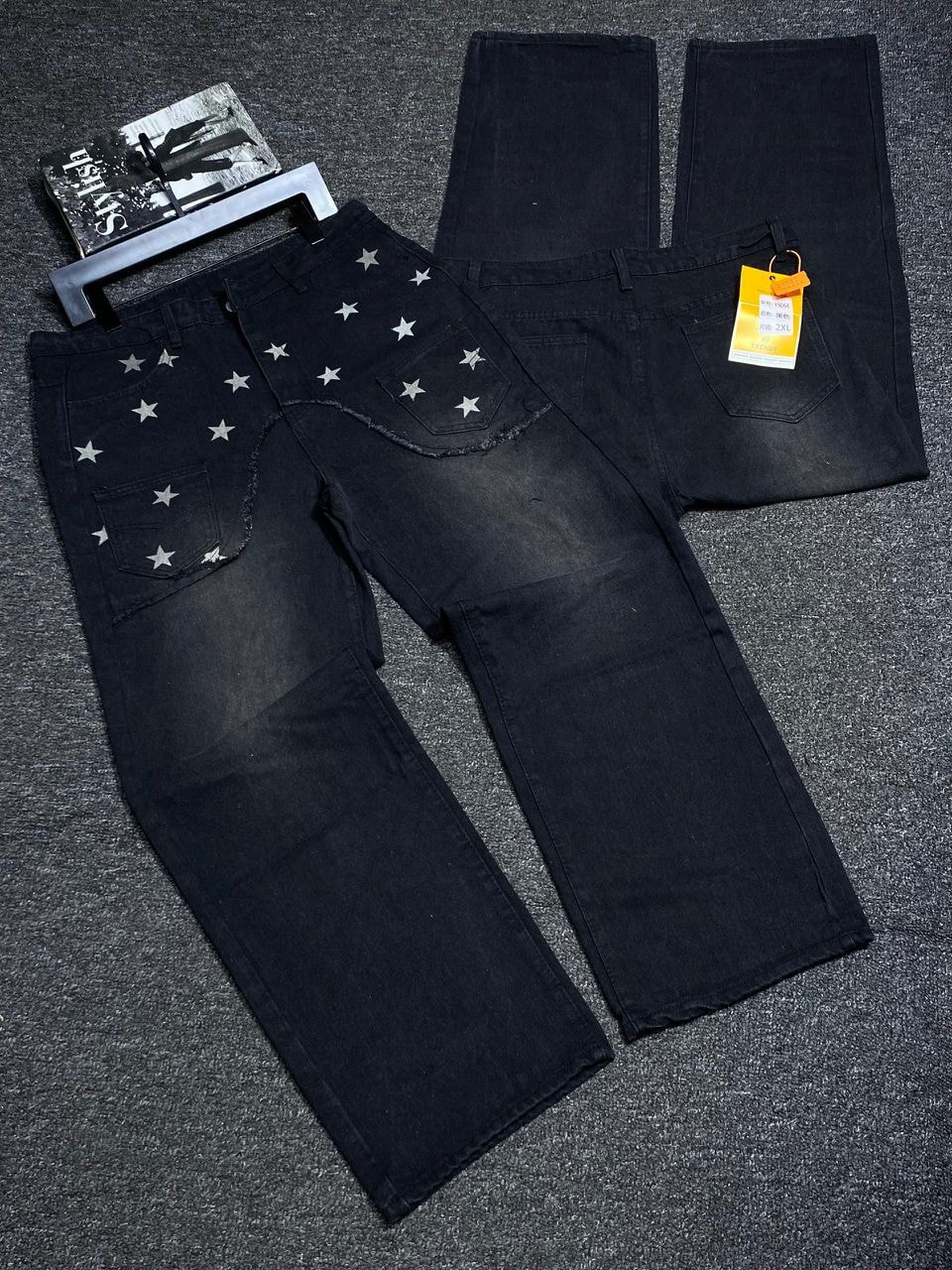 Flat lay of black baggy jeans showing back with silver star prints, pockets and size tags.
