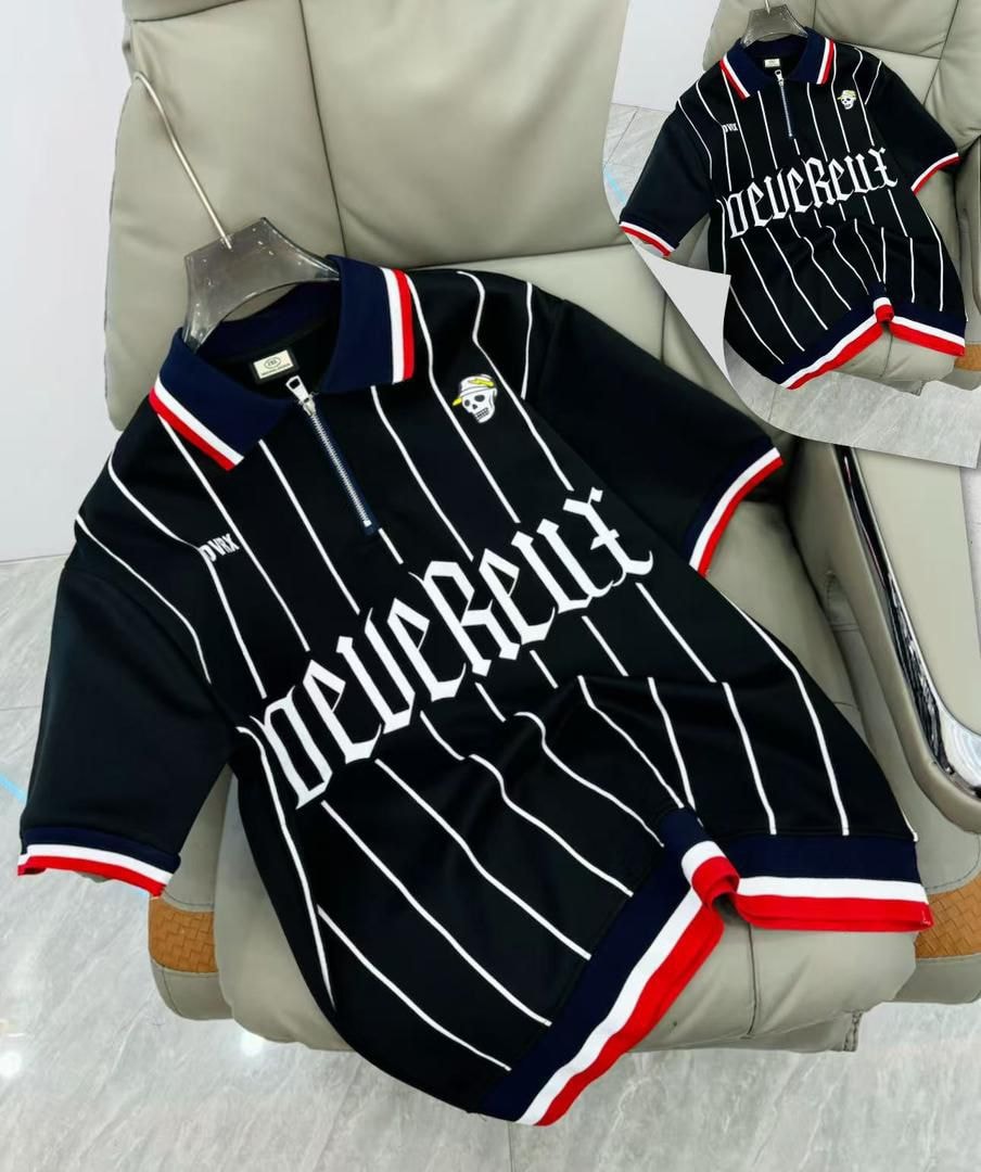 Black striped polo shirt with gothic lettering, skull detail, and contrasting trims on a leather chair.